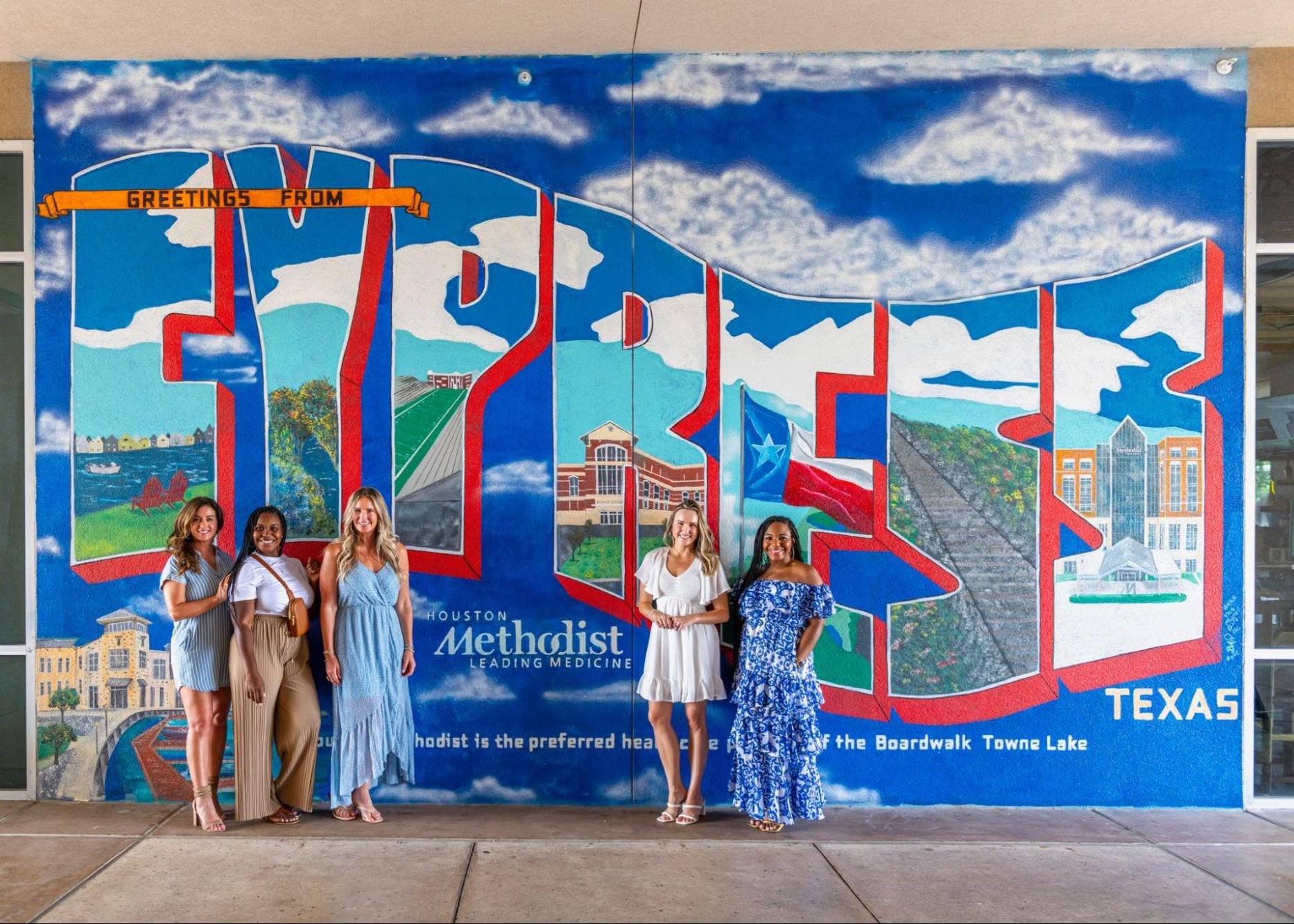 Visitors posing in front of the Cypress mural at The Boardwalk Towne Lake in Cypress, Texas.